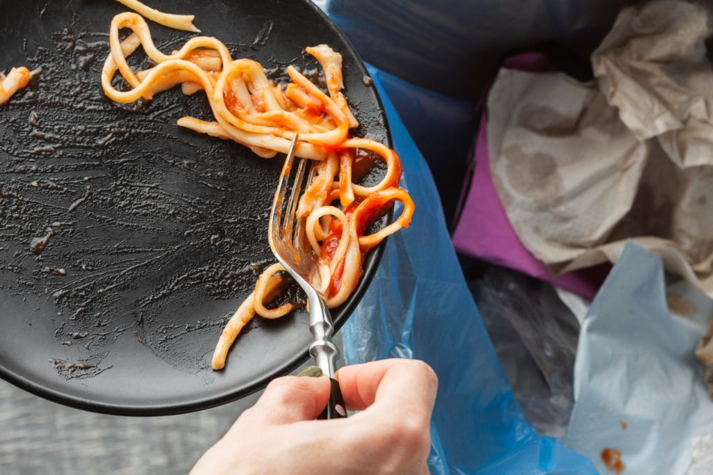 Scena marnowania jedzenia - spaghetti wyrzucane z talerza do kosza.